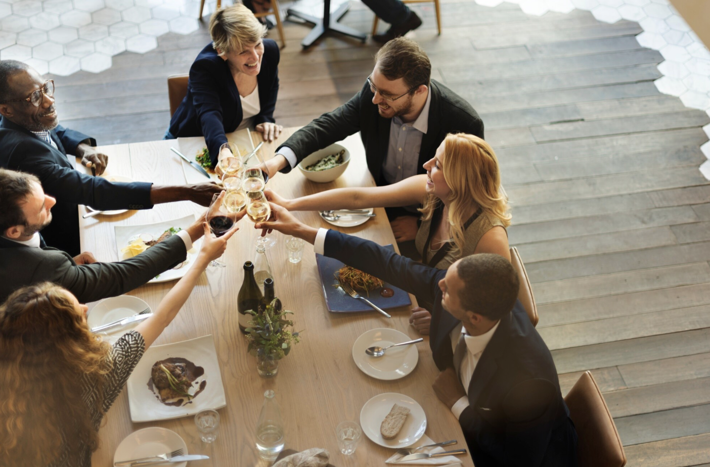 Cette image montre un groupe de collègues réunis autour d’un repas dans un cadre convivial et chaleureux. Ils lèvent leurs verres pour trinquer, souriants et détendus, suggérant un moment de célébration ou de cohésion d’équipe. L’ambiance est professionnelle mais festive, typique d’un déjeuner d’entreprise, d’un repas de fin d’année ou d’un événement CSE.